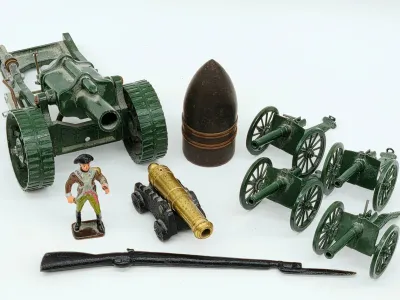 Collection of vintage toy military items, including Britains-style die-cast green cannons, a brass cannon model, a lead soldier figure, a...