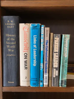 Collection of vintage military history books, including titles on World War II and military strategy, displayed on a wooden shelf.