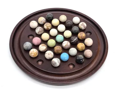 Vintage wooden solitaire board game featuring a collection of polished semi-precious gemstone marbles in various colors and patterns.