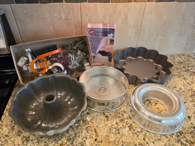 Assorted baking pans and accessories, including a fluted bundt pan, a springform pan, a ring mold, a scalloped tart pan, a box of cookie...