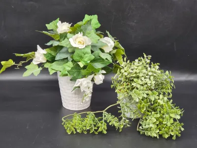 Two artificial potted plants, including one with white roses and ivy in a textured white ceramic pot, and another with cascading green...