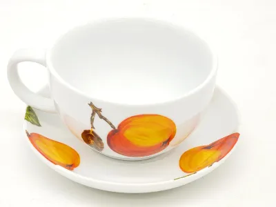 White ceramic teacup and saucer set featuring hand-painted fruit motifs in warm orange, yellow, and brown tones.