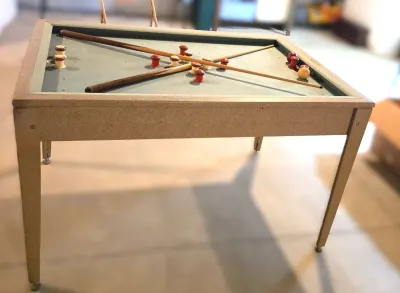 Vintage bumper pool table with a speckled laminate frame, complete with cues, balls, and bumpers.
