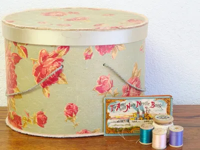 Vintage floral fabric-covered hat box with a cord handle, paired with an antique "The Army and Navy Needle Book" and several...