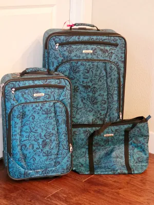 Three-piece American Tourister luggage set in a teal and black floral pattern, including two rolling suitcases and a matching tote bag.
