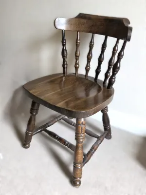 Vintage dark-stained wooden captain's chair featuring turned spindle backrests and legs with a contoured seat.