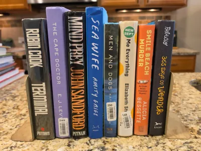 A collection of eight hardcover and paperback fiction books, including titles by Robin Cook and John Sandford, standing upright between...