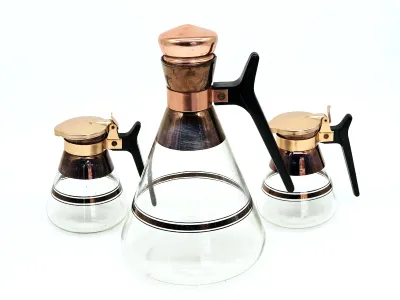 Vintage mid-century modern glass carafe and matching creamer and sugar set, featuring copper-toned metal accents and black plastic handles.
