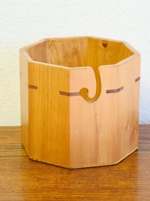 Octagonal wooden yarn bowl with a natural finish, featuring a carved spiral guide slot and dark wood inlay accents.