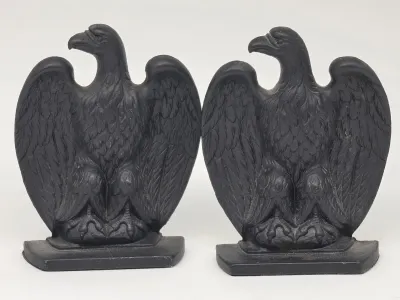 Pair of vintage cast iron eagle bookends with a matte black finish, featuring detailed feathering and a classic patriotic motif.