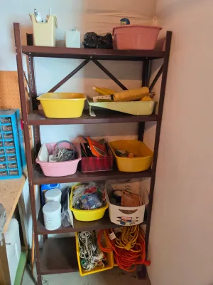 Five-tier brown metal shelving unit holding various garage and workshop supplies, including plastic bins, painting tools, and extension...