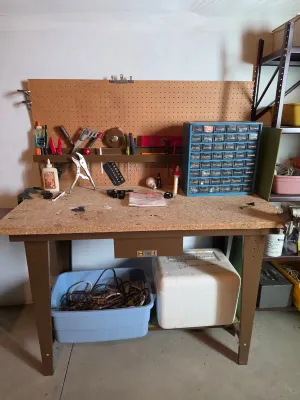 Hirsh metal workbench with a particle board top, integrated pegboard backing, and a small center drawer, shown with various hand tools...