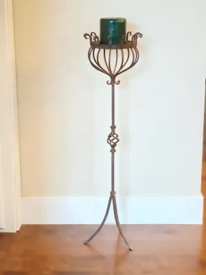 Wrought iron floor-standing candle holder with a tripod base, twisted metal accent, and a green pillar candle.