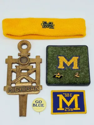 Collection of vintage University of Michigan memorabilia, including a brass key-shaped plaque, a yellow headband, a "Go Blue"...