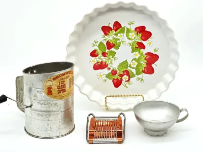 Vintage kitchenware set featuring a Bromwell 3-cup crank sifter, a ceramic strawberry-patterned fluted tart dish, a copper-toned egg...