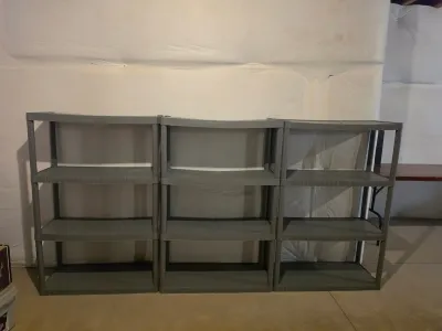 Three matching grey plastic four-tier utility shelving units, showing some slight bowing on the top shelves.