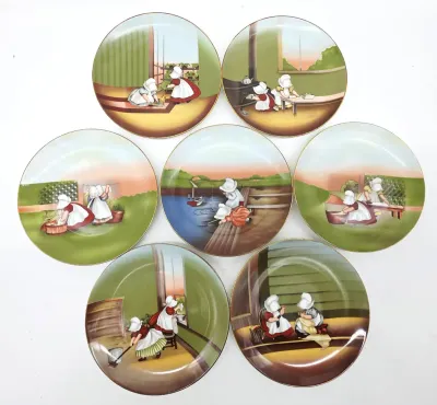Set of seven vintage porcelain collector plates featuring Sunbonnet Sue illustrations depicting various household chores and outdoor...