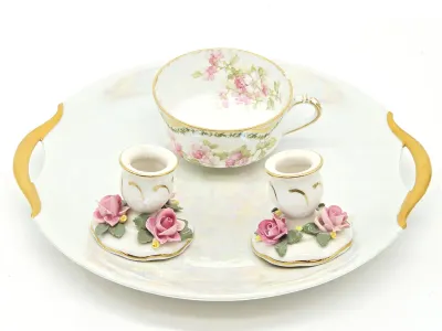 Vintage porcelain vanity set featuring a handled tray with an iridescent finish, a floral teacup, and a pair of small candlesticks...