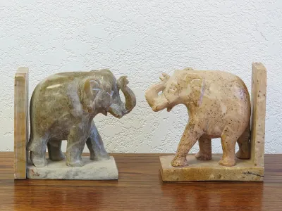 Pair of hand-carved stone elephant bookends, featuring one in a polished greenish-gray soapstone and the other in a textured beige marble.