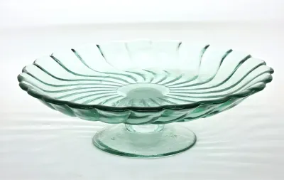 Vintage light green glass pedestal cake stand featuring a scalloped rim and a molded swirl pattern.