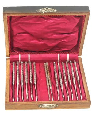 Antique set of twelve silver-plated nut picks with textured handles, presented in a red satin-lined wooden storage box.