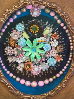 Vintage costume jewelry art piece featuring an assortment of mid-century enamel flower brooches, beads, and rhinestones arranged in a...