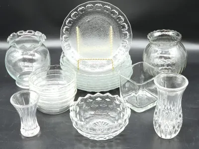Assorted clear glassware collection, including a stack of apple-patterned plates, small bowls, and various decorative vases.