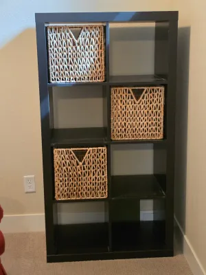 Black-brown IKEA Kallax 2x4 cube organizer shelf unit, complete with three woven seagrass storage baskets.