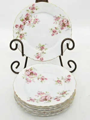 Set of Haviland Limoges porcelain plates featuring a delicate pink rose pattern with scalloped, gold-gilded rims, displayed on a black...