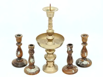 Vintage brass pricket candlestick holder with a wide drip pan, flanked by two pairs of turned wooden candlesticks showing heavy wax residue.