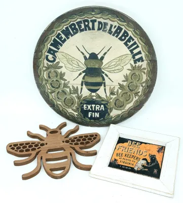 Bee-themed decor trio featuring a round wooden Camembert de L'Abeille sign, a wooden honeybee trivet, and a framed vintage-style Bee...