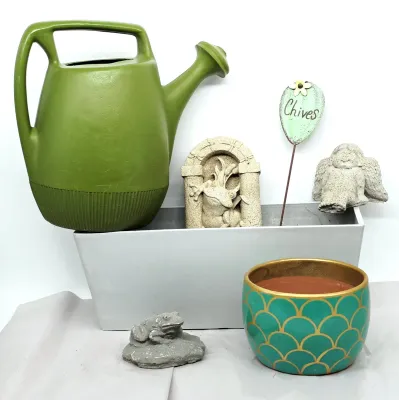 Assorted garden decor including a green plastic watering can, a grey rectangular planter, a teal and gold scalloped ceramic pot, a...