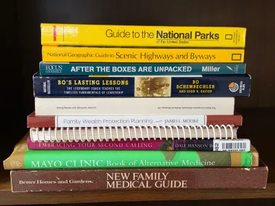 Stack of non-fiction books including National Geographic guides, medical reference books, and self-help titles, showing some wear from use.