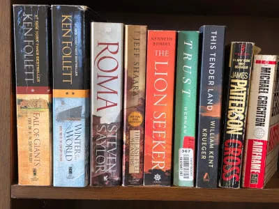 Selection of popular fiction and historical novels on a wooden shelf, including titles by Ken Follett, James Patterson, and Michael...