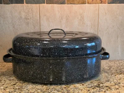 Vintage black speckled enamelware roasting pan with matching lid, showing minor wear consistent with age.