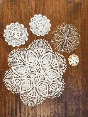 Collection of five vintage handmade crochet doilies in various sizes and intricate patterns, displayed on a wooden floor.
