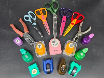 Assortment of crafting tools, including decorative edge scissors, hand punches, and various paper shape punches, featuring a Disney...