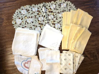 Assortment of vintage table linens, including a cutwork floral runner, yellow cloth napkins, and various embroidered white handkerchiefs...