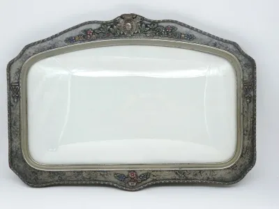 Vintage white porcelain serving platter set in an ornate, tarnished metal frame featuring floral details and a crest at the top.
