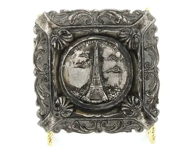 Vintage silver-tone metal souvenir ashtray featuring a central relief of the Eiffel Tower, enclosed in an ornate, scroll-decorated square...