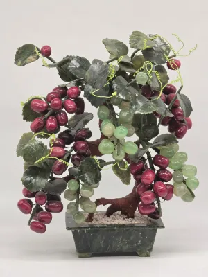Vintage Chinese jade and agate bonsai tree featuring clusters of purple and green grapes with carved stone leaves, set in a dark green...