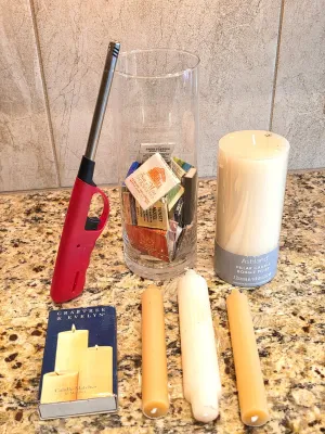 Assortment of candles and lighting accessories, including an Ashland pillar candle, a glass cylinder vase filled with vintage matchbooks,...