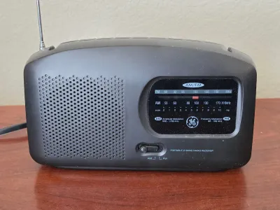 Vintage General Electric portable 2-band AM/FM radio receiver in a black plastic casing, featuring a telescoping antenna and manual...