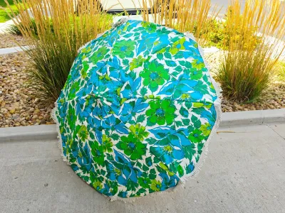 Vintage 1960s or 1970s patio umbrella featuring a vibrant blue and green floral pattern with white fringe trim.