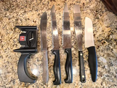 Wüsthof handheld knife sharpener shown alongside an assortment of kitchen knives, including a wooden-handled utility knife, serrated...