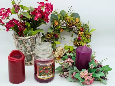 Assorted home decor items including a Yankee Candle in Red Apple Wreath scent, two pillar candles, a woven basket vase with faux red...