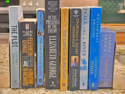 A collection of nine fiction books, including titles by Elizabeth George and William Kent Krueger, held together by metal bookends on a...
