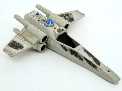 Vintage Kenner Star Wars X-Wing Fighter toy, showing battle damage decals and missing its canopy and laser cannons.