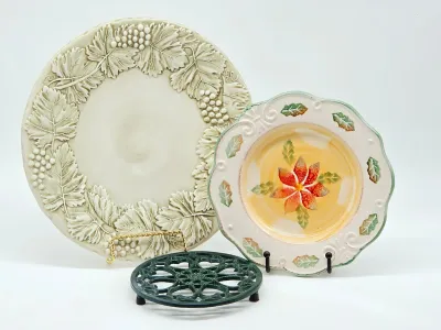 Two decorative ceramic plates, one featuring a raised grape and leaf border and the other a hand-painted poinsettia motif, shown with a...
