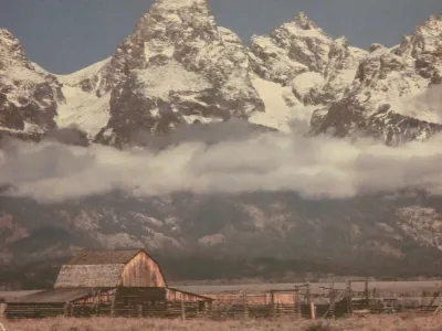 Vintage landscape photograph depicting the Moulton Barn in Grand Teton National Park, featuring snow-capped mountains and low-hanging...
